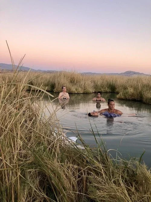 Three women resting in a desert hot spring at dusk